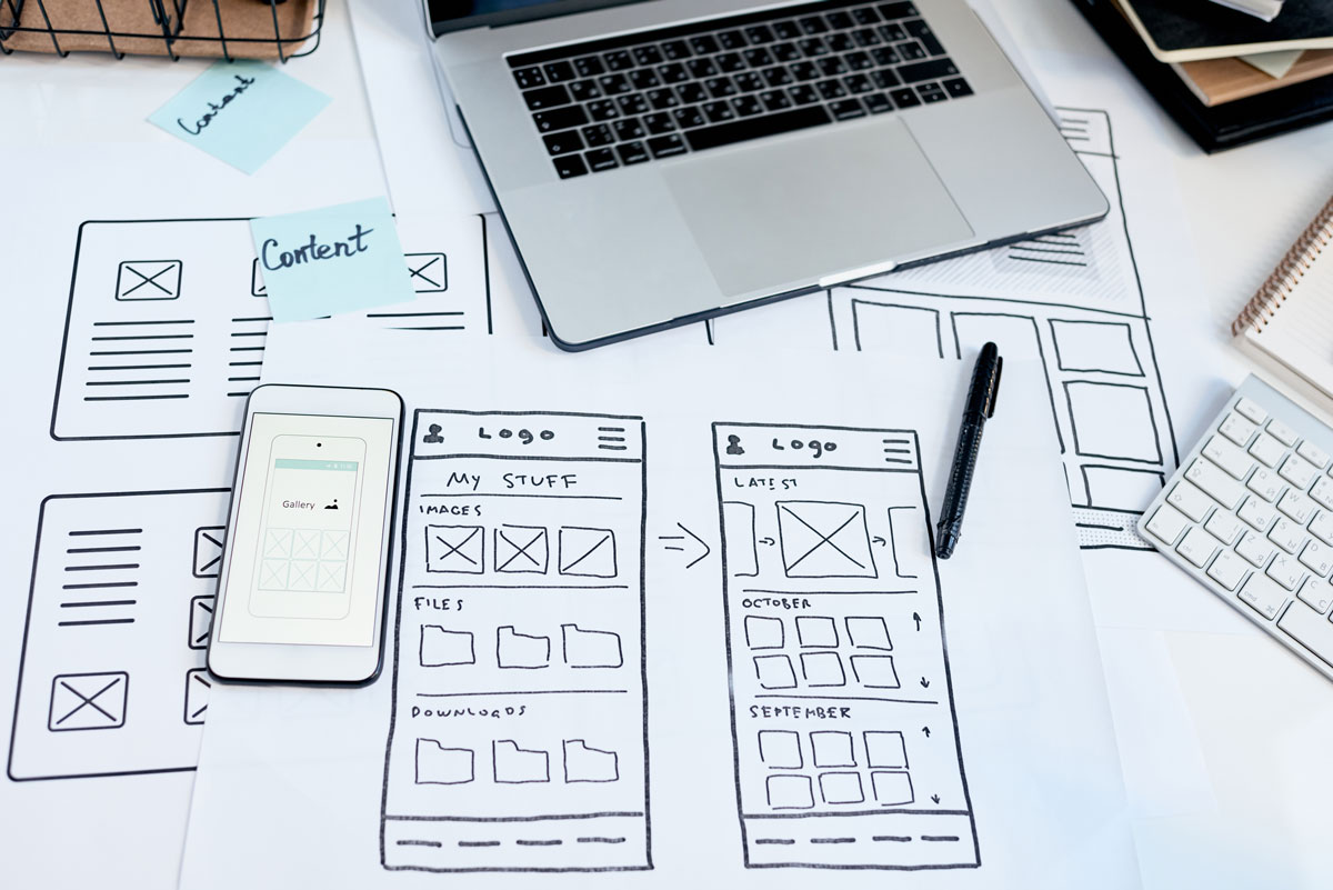 Laptop, Smartphone und gezeichnete Website-Wireframes auf einem Schreibtisch